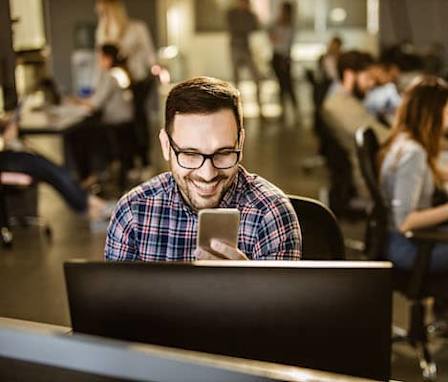 Man smiling at smartphone while working in office